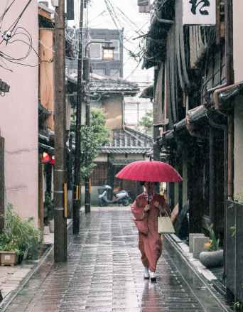 woman in brown robe holding umbrella walking on concrete pathway