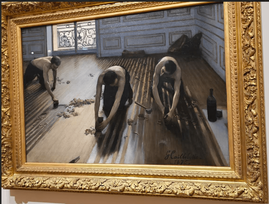 A painting by Gustave Caillebotte depicting three men working on a wooden floor, with tools and debris scattered around. The men are shown from the waist up, wearing shirts and focused on their task, while a wine bottle is visible in the foreground.