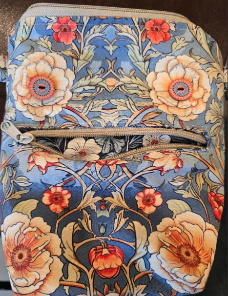 Floral blue fabric pouch with zipper and large cream, red, and orange flowers. There are two buttons in the flowers above the zipper, making them look like eyes.